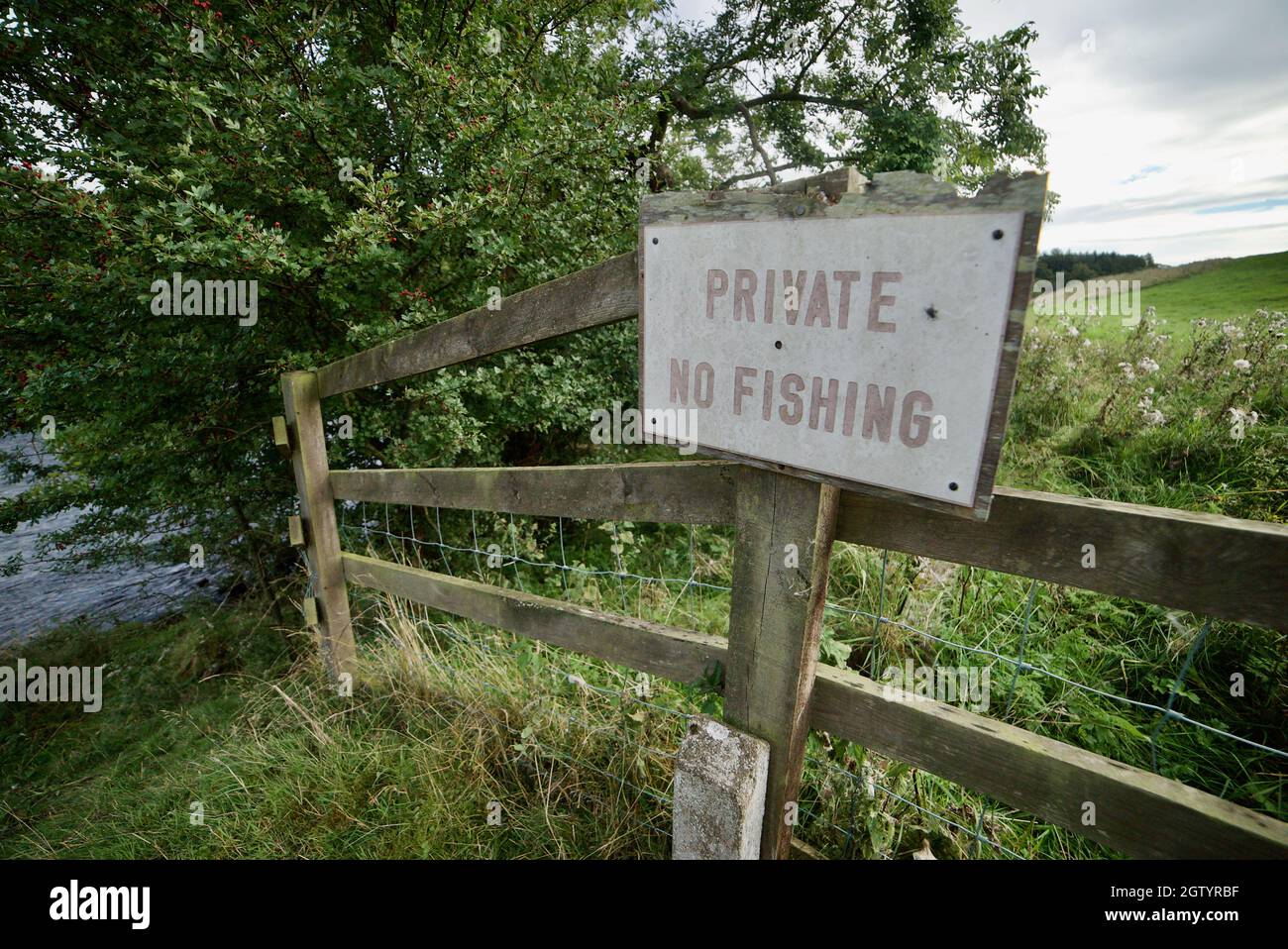 PRIVATE- NO FISHING sign on a fence next to a river/stream in Northumberland, UK. A wooden fence with a sign post saying 'Private No Fishing'. Stock Photo