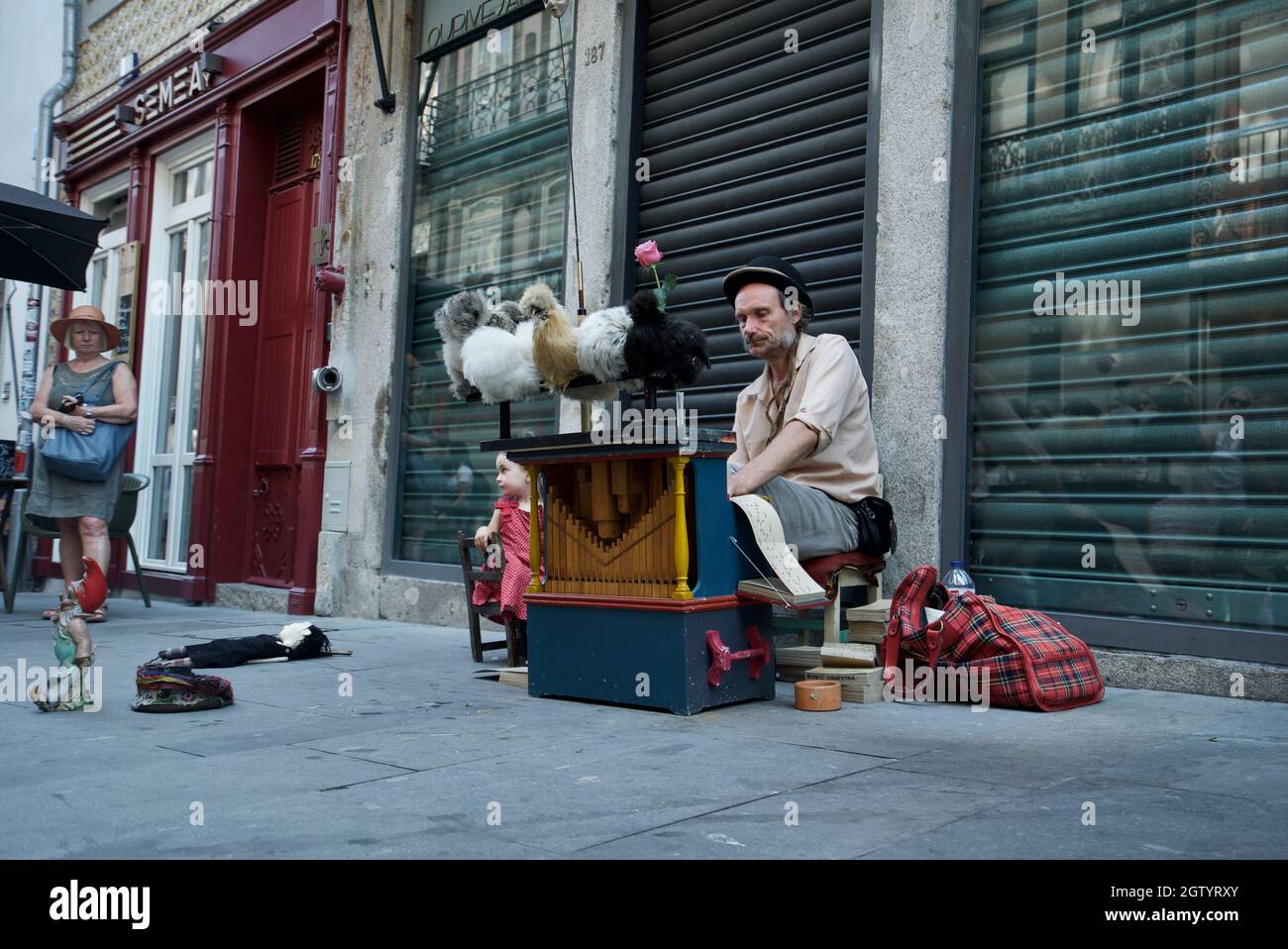 Busker playing a card based music box with chickens at Rua das Flores, Porto - Portuguese street busker playing organ instrument with Silkie Chickens Stock Photo
