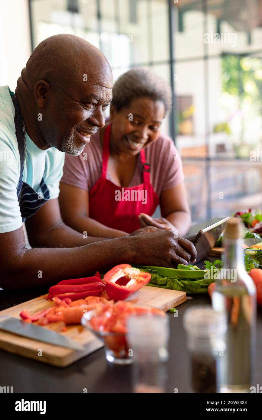 Happy african american senior couple cooking together in kitchen, using ...