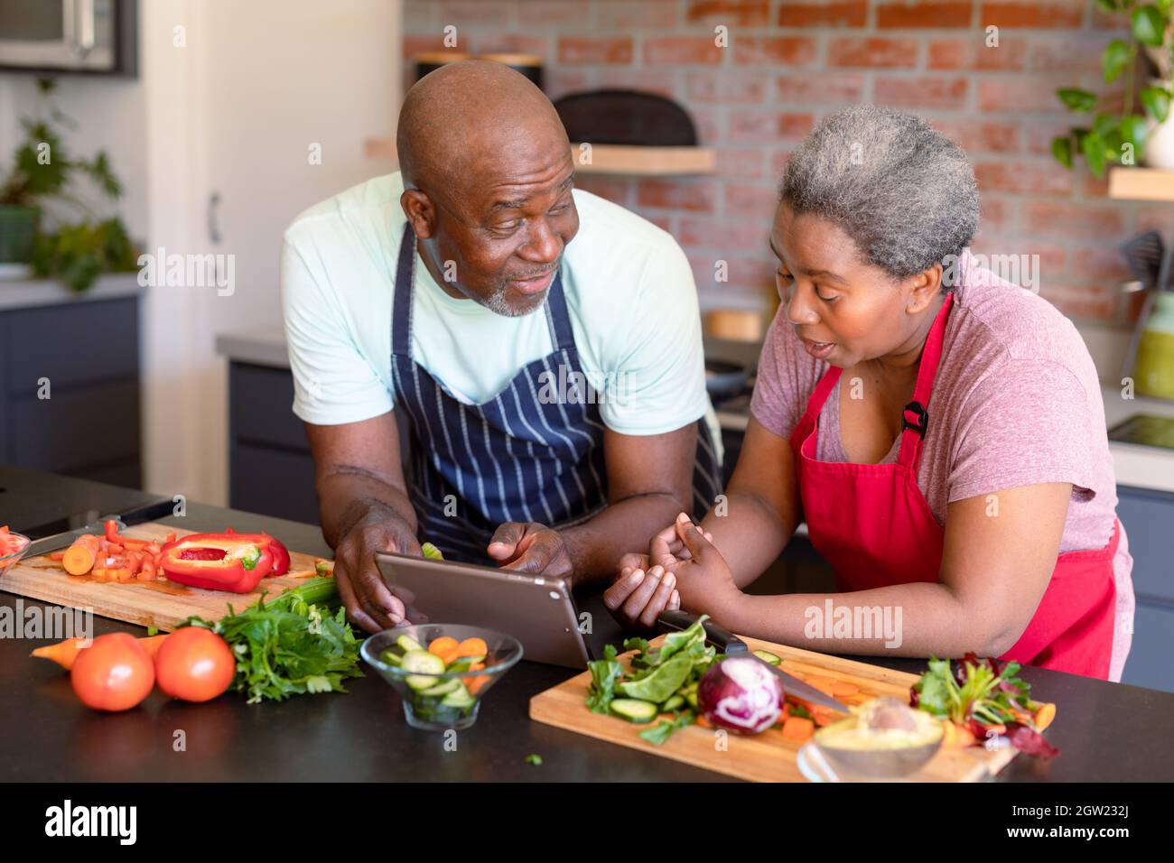 Happy african american senior couple cooking together in kitchen, using ...