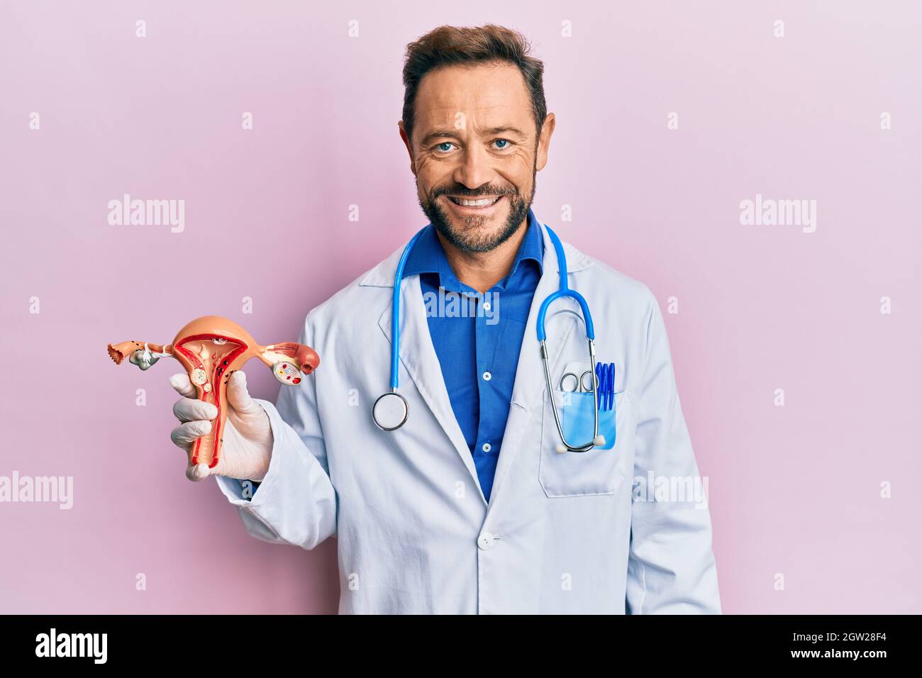 Middle age gynecologist man holding anatomical model of female genital organ looking positive and happy standing and smiling with a confident smile sh Stock Photo