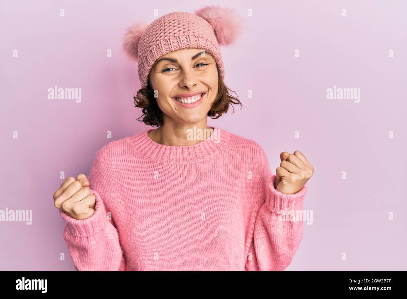 Young brunette woman wearing cute wool cap celebrating surprised and amazed for success with arms raised and open eyes. winner concept. Stock Photo