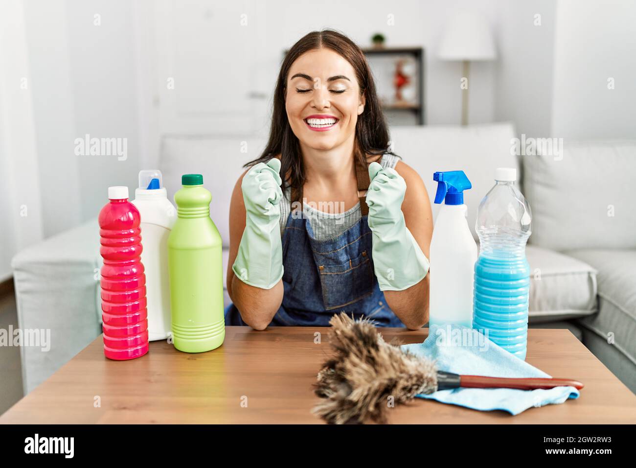 Young brunette woman wearing cleaner apron and gloves cleaning at home ...