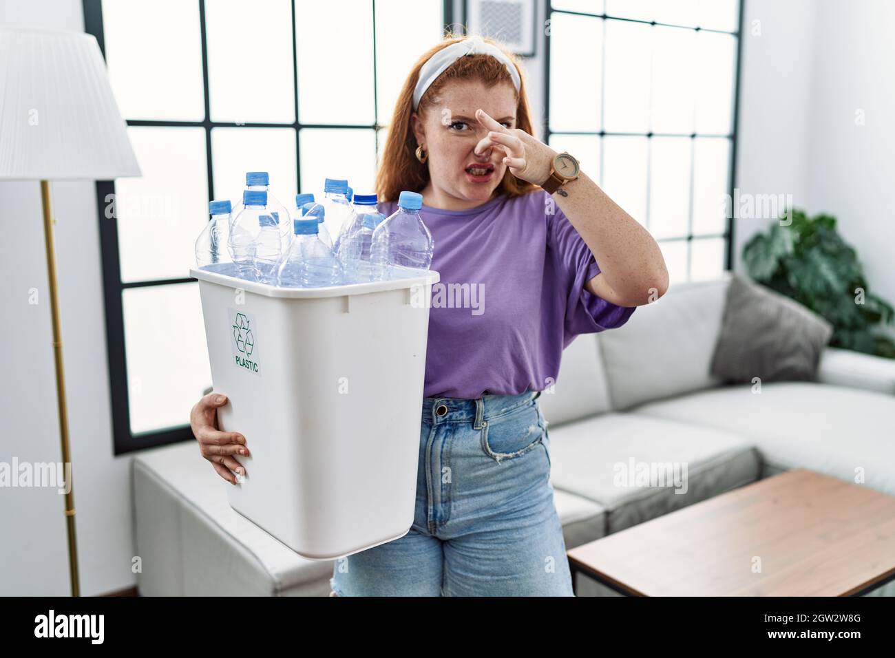 Young redhead woman holding recycling wastebasket with plastic bottles ...