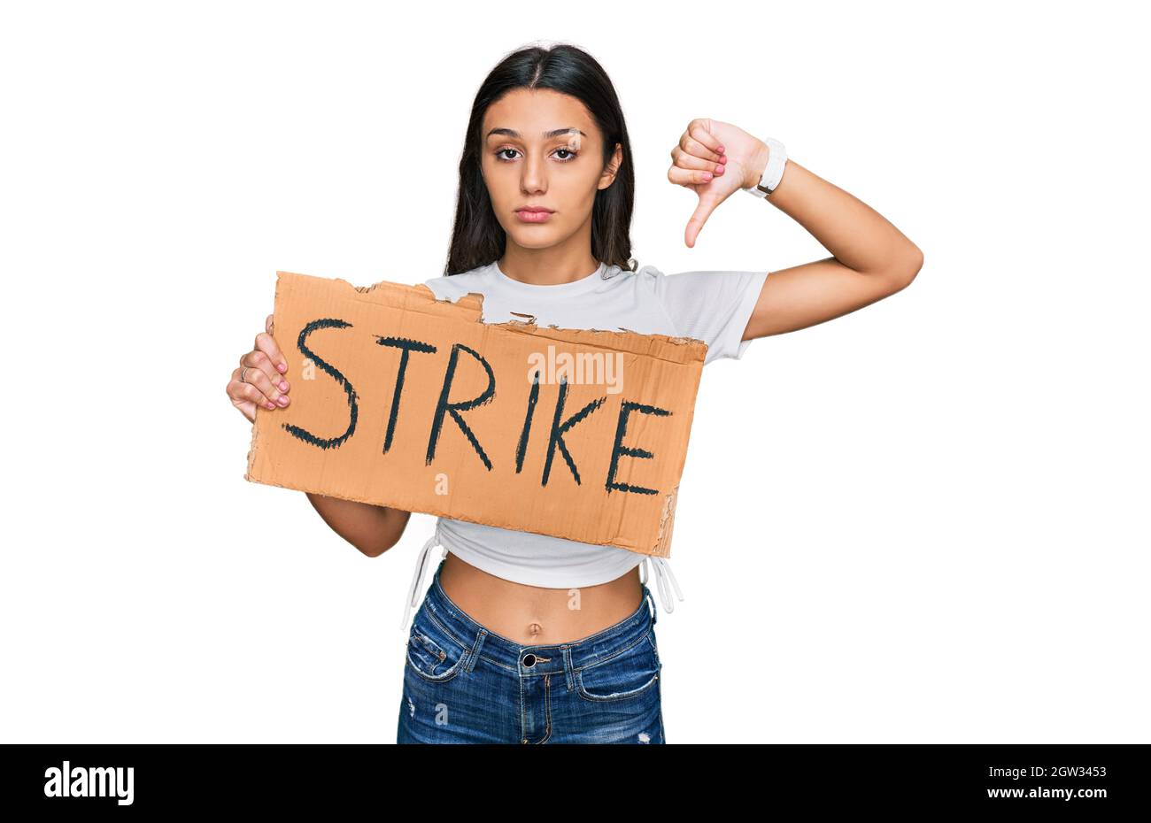 Young hispanic girl holding strike banner cardboard with angry face, negative sign showing dislike with thumbs down, rejection concept Stock Photo