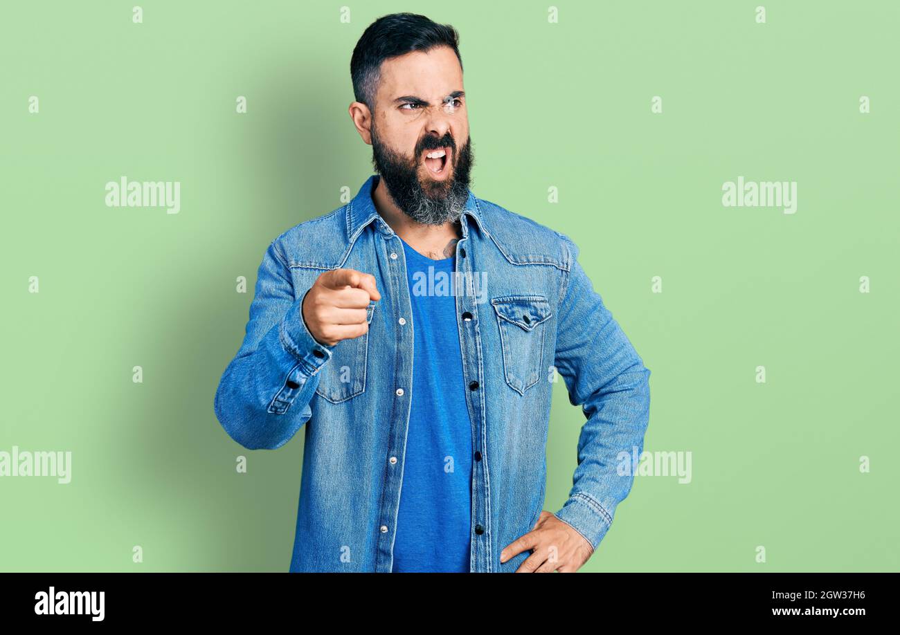 Hispanic man with beard pointing with finger to camera angry and mad screaming frustrated and furious, shouting with anger. rage and aggressive concep Stock Photo