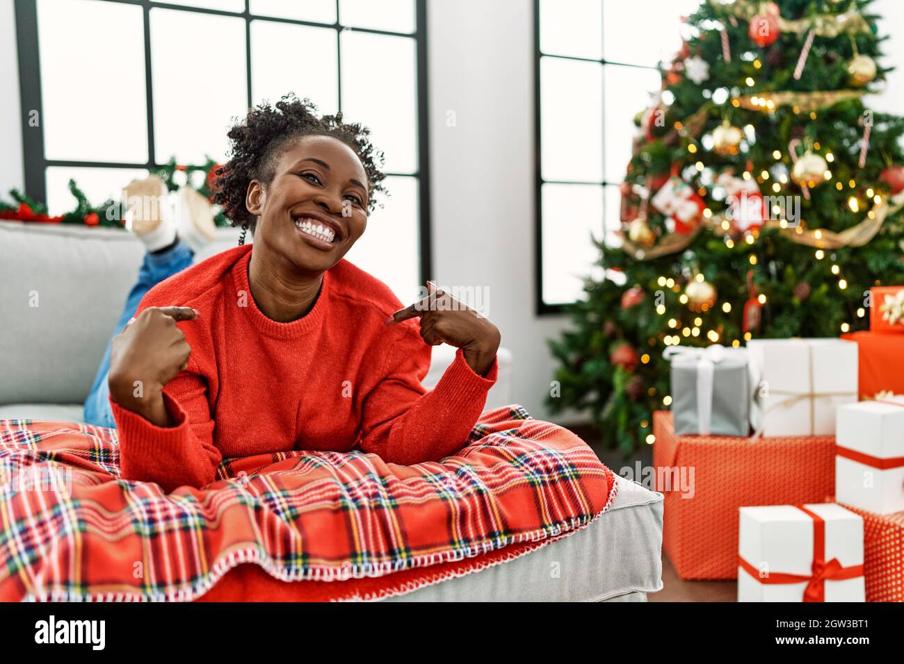 Young african american woman lying on the sofa by christmas tree ...