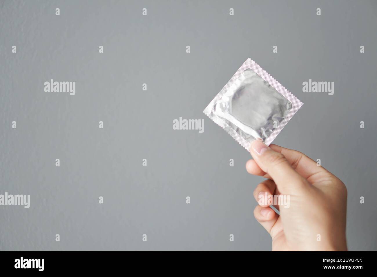 Close-up Of Hand Holding Condom Against Gray Background Stock Photo