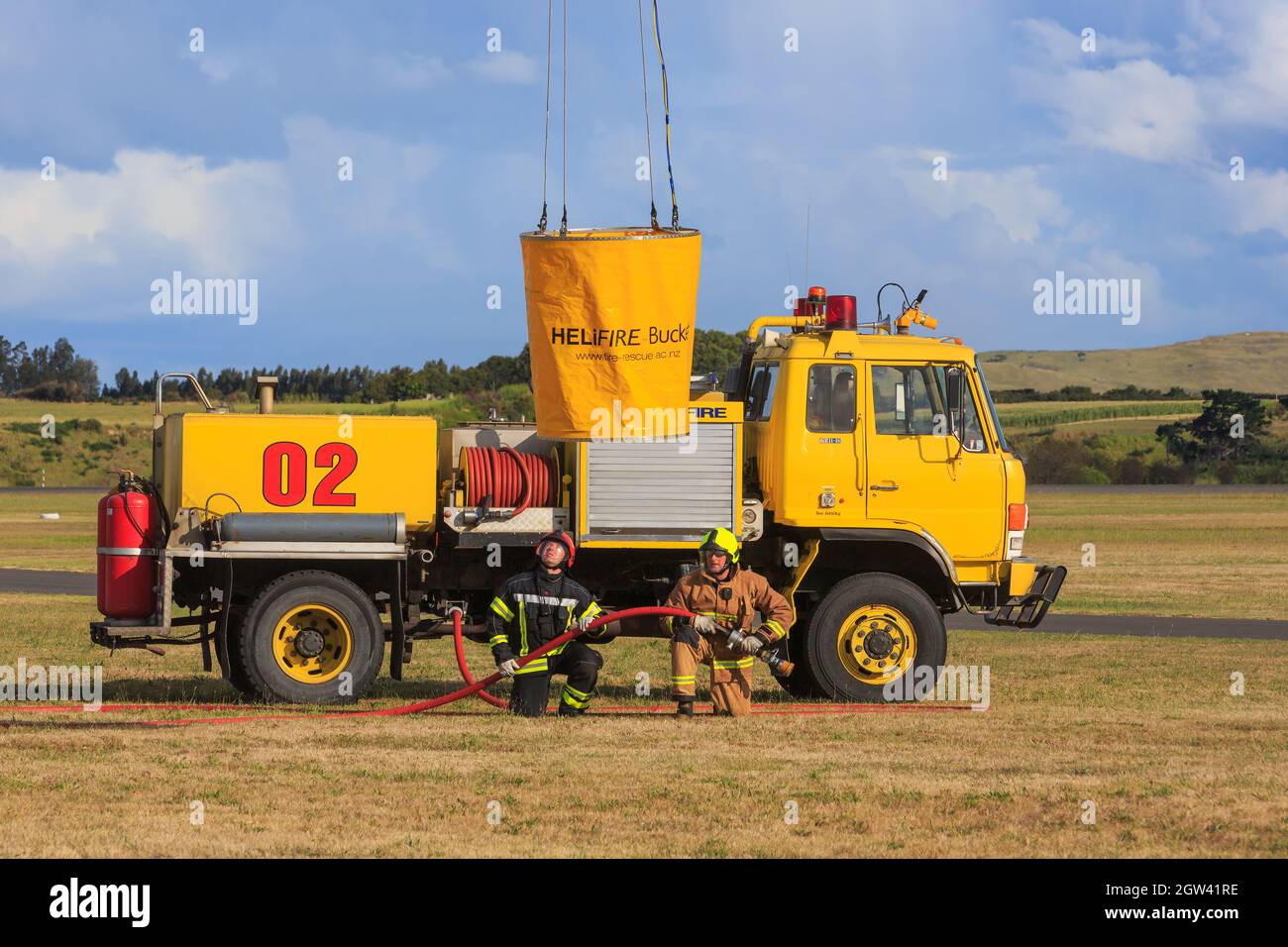 A fire truck at an airport. A monsoon bucket is being lowered by a helicopter for the firefighters to fill Stock Photo