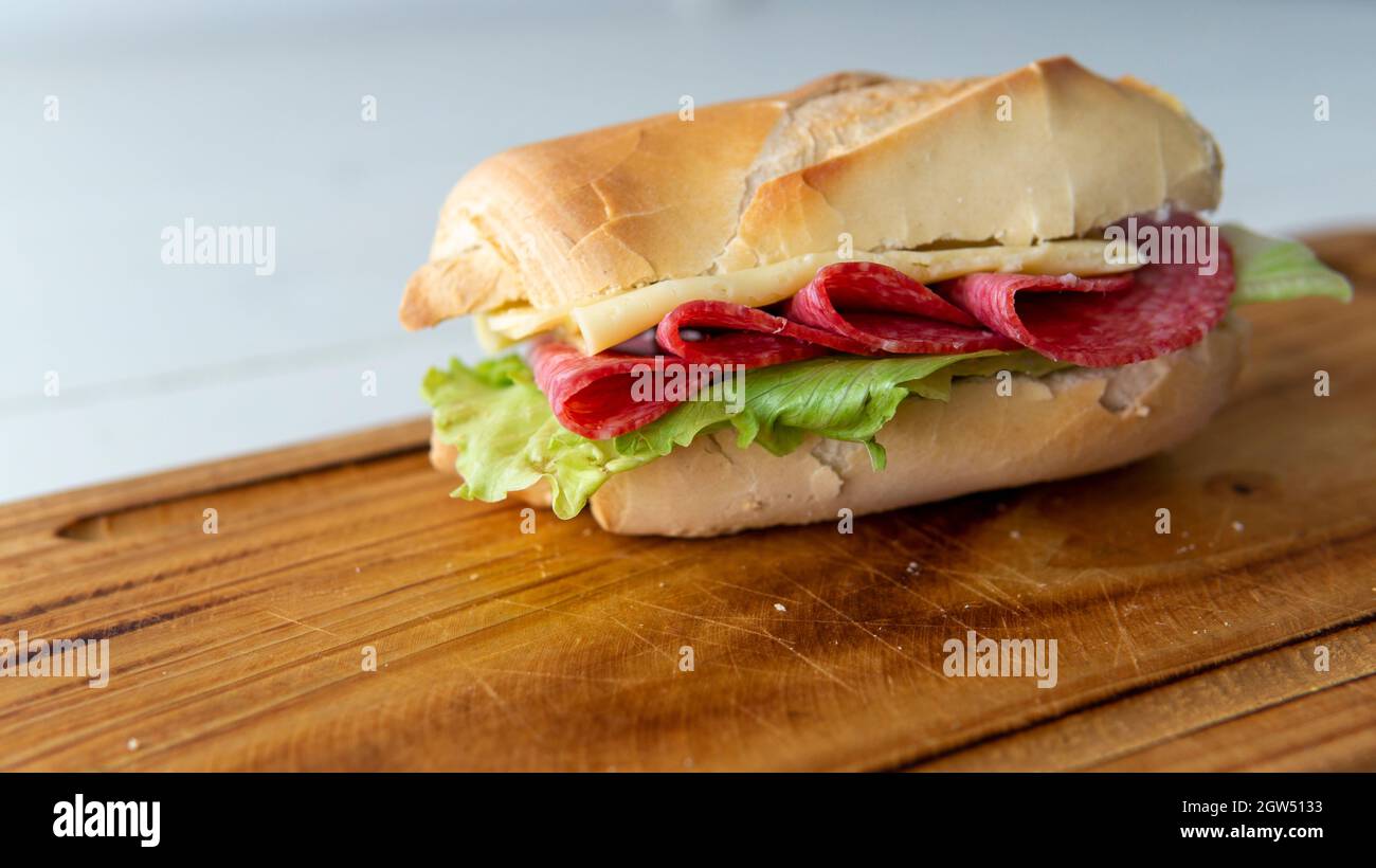 Close view of a homemade salami, cheese and lettuce sandwich, on top of a wooden plate Stock Photo
