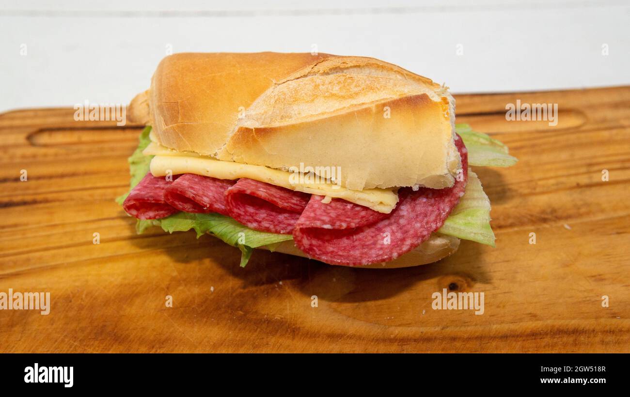 Close view of a homemade salami, cheese and lettuce sandwich, on top of a wooden plate Stock Photo
