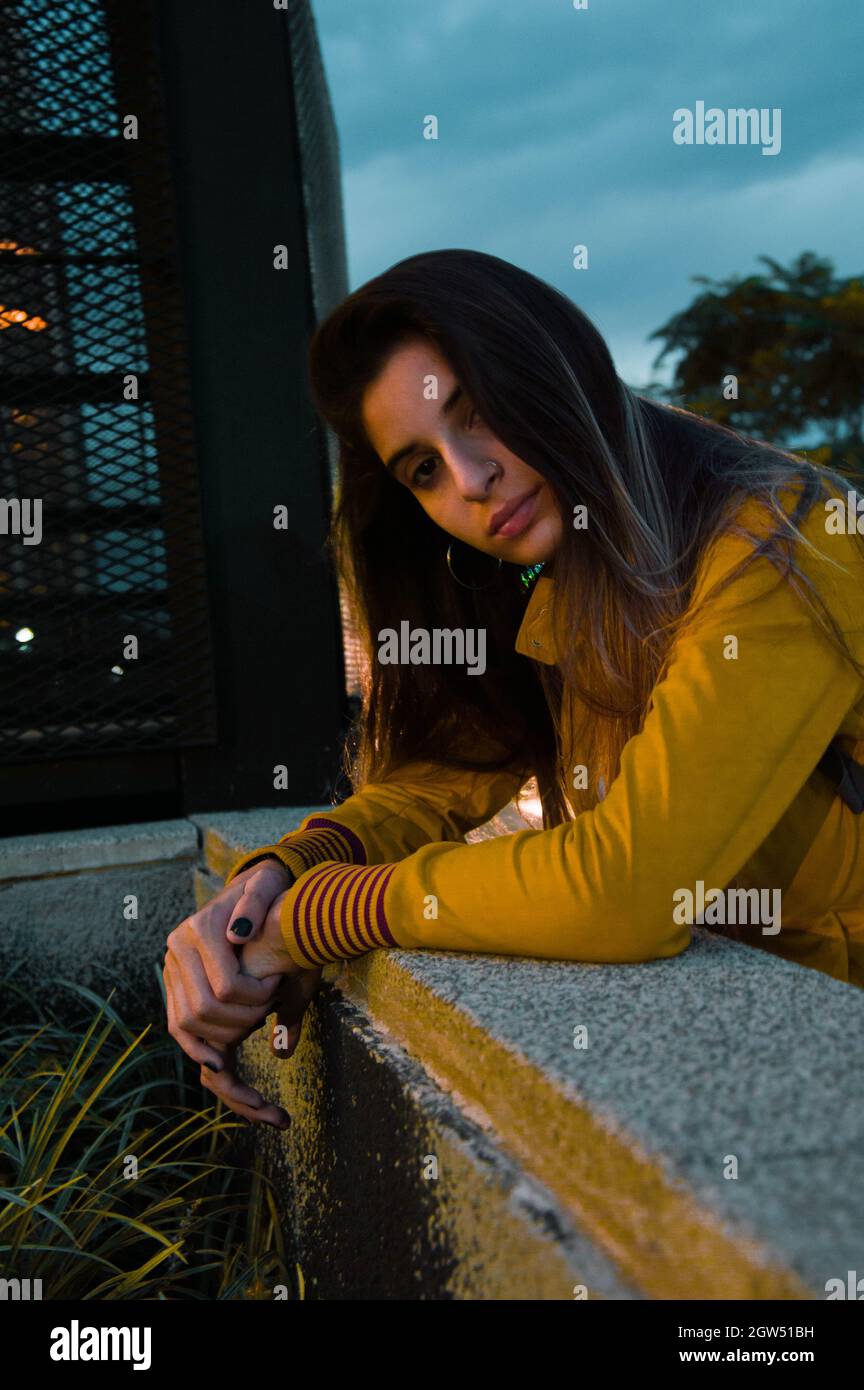 Portrait Of Young Woman Standing By Retaining Wall At Dusk Stock Photo