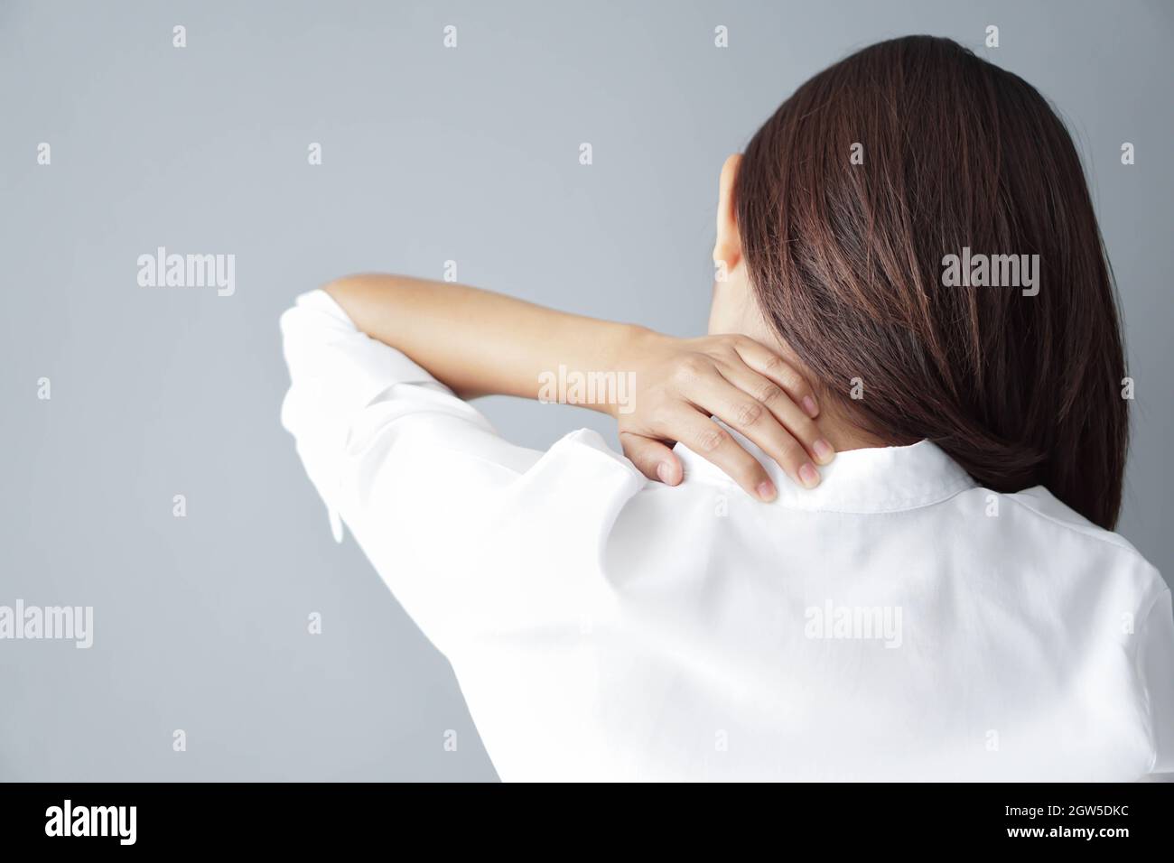 Rear View Of Woman Having Neckache Against Gray Background Stock Photo