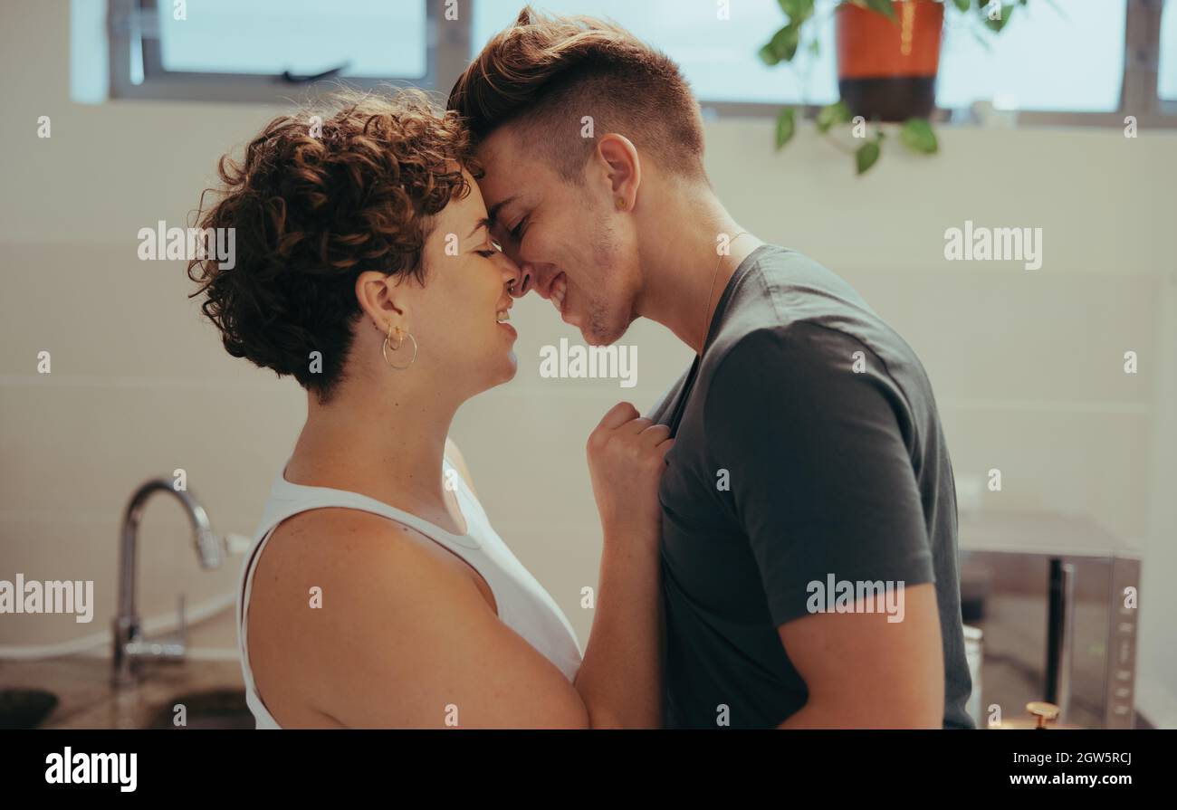 Affectionate queer couple being romantic at home. Happy young couple smiling while touching their foreheads together. Romantic young LGBTQ+ couple bon Stock Photo