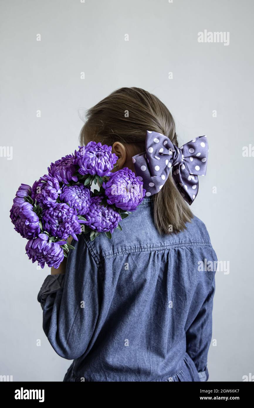 Little girl with a beautiful bow on her hair holds a bouquet of blue ...