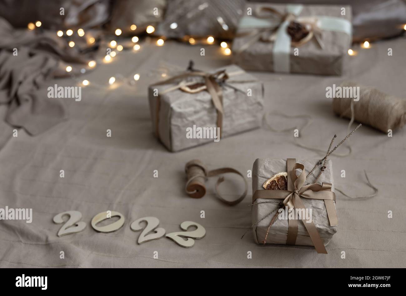 Christmas background with gift boxes wrapped in craft paper and wooden numbers 2022 on blurred background with garland. Stock Photo