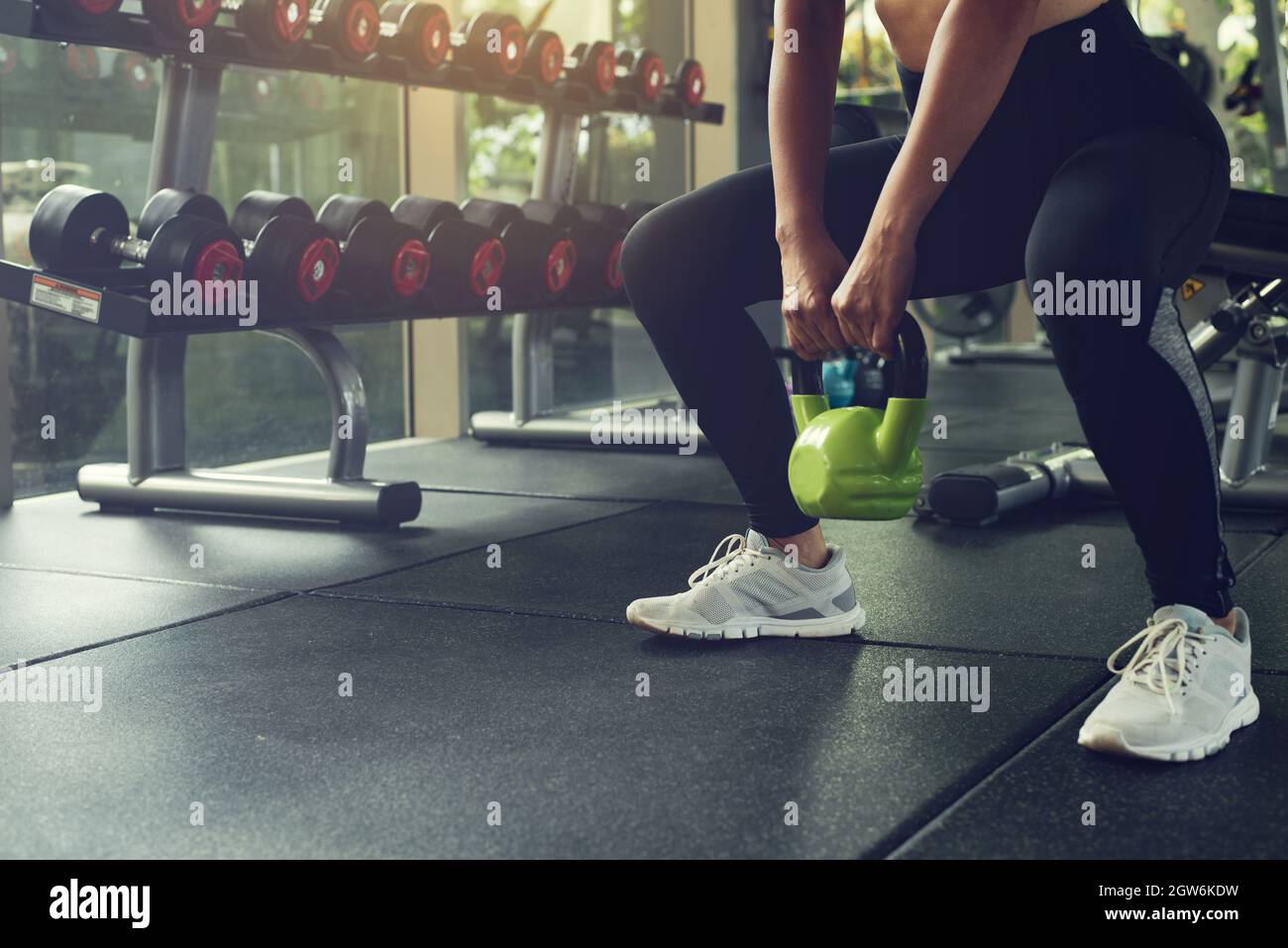 Woman exercising with kettlebell while being in squats position at the gym. Stock Photo