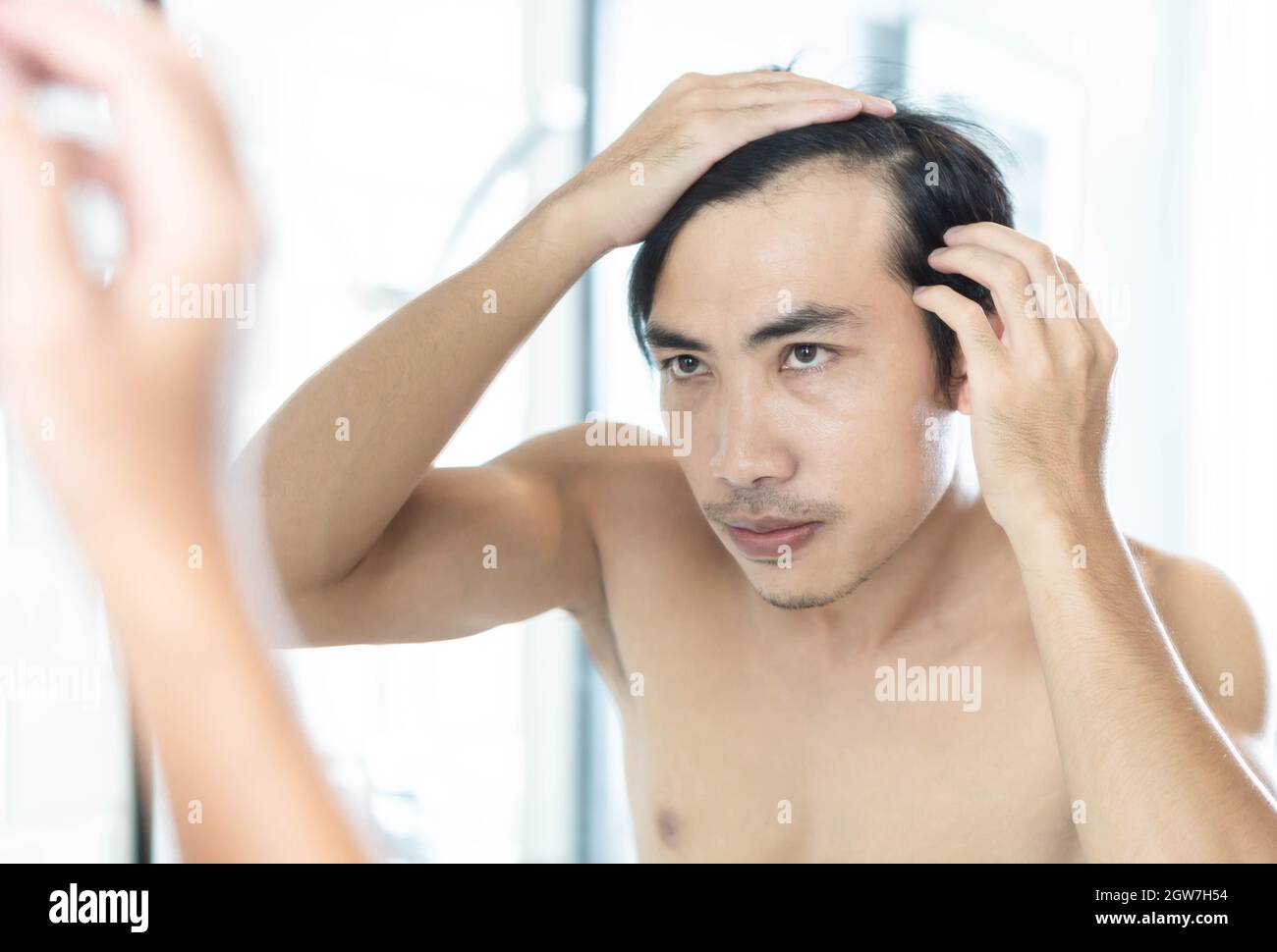 Mid Adult Man Looking In Mirror While Touching His Receding Hairline At Bathroom Stock Photo