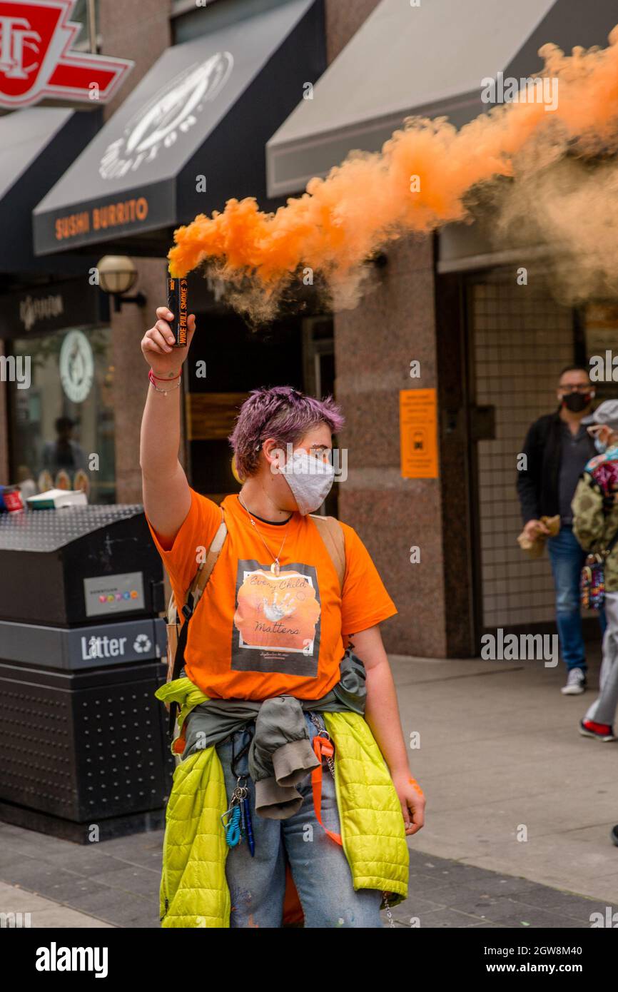 A participant holds a yellow smoke flare during the Orange Shirt Day and National Day of Truth and Reconciliation at Dundas Square, to heal, raise awareness and rise together as an Indigenous Community.Organized by Matriarchal Circle, a Toronto-based grassroots organization impacted by child welfare agencies. The Matriarchal Circle's vision is for child welfare to be practiced in Toronto in true Indigenous grassroots led circles, 'as opposed to the neo-colonial, oppressive, genocidal acts in the current child welfare system. Stock Photo