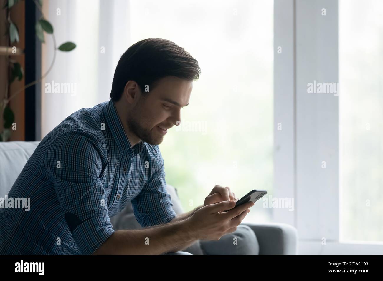 Side view smiling man using smartphone, sitting on cozy couch Stock Photo