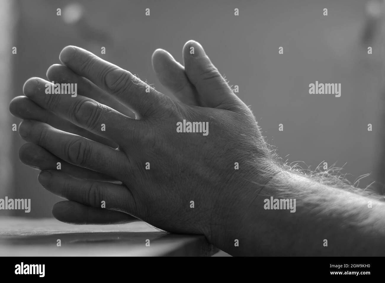 Defocus, blur, noise, grain effect. Close-up of men's hands folded in prayer. Hands of an elderly man lying on the table. Side view. Monochrome. Selec Stock Photo