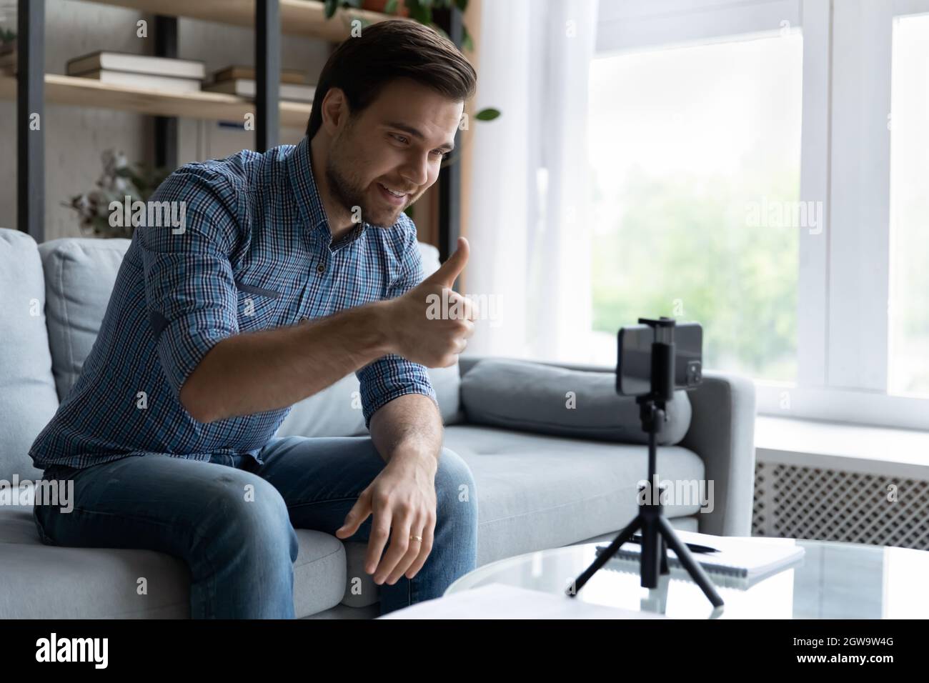 Smiling man showing thumb up, using smartphone on tripod Stock Photo