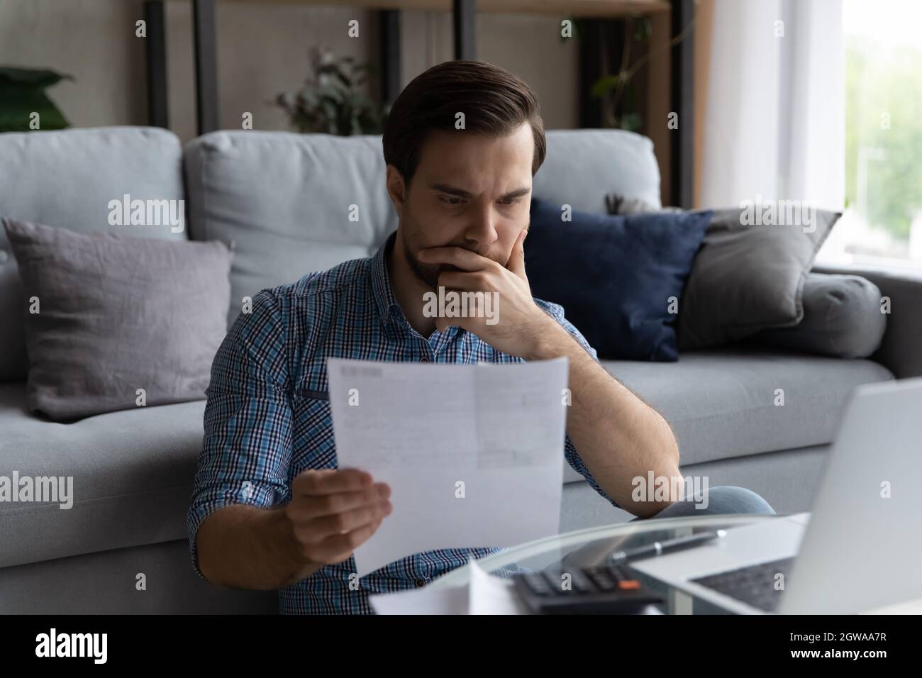 Thoughtful man checking financial documents, calculating bills, using laptop Stock Photo