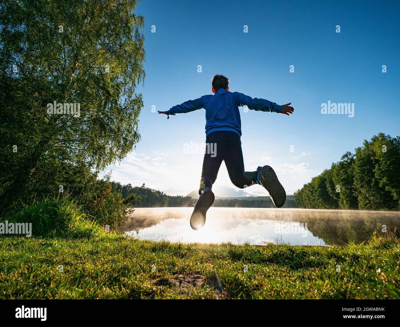 Fast Jumping Short Hair Boy At Mountain Lake Makes A Fun. Careless Childhood Concept Image. Stock Photo