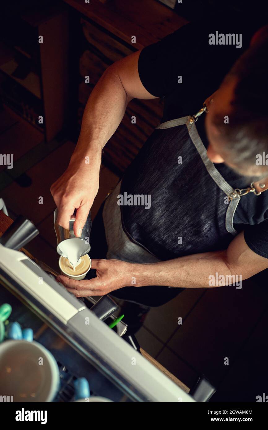 pouring steamed milk to a cappuccino cup. professional coffee bar worke Stock Photo