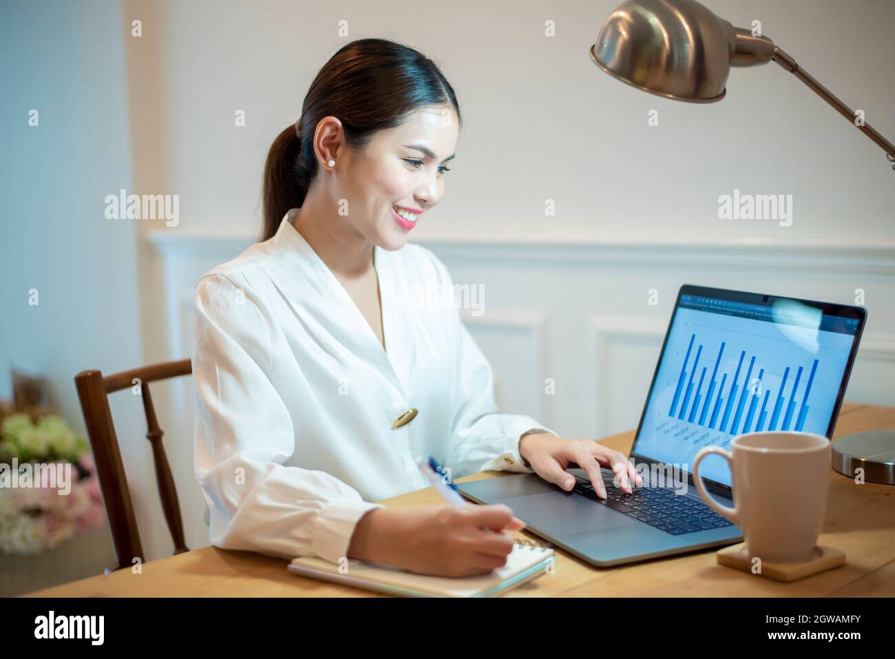 Smiling Woman Using Laptop While Sitting At Office Desk Stock Photo