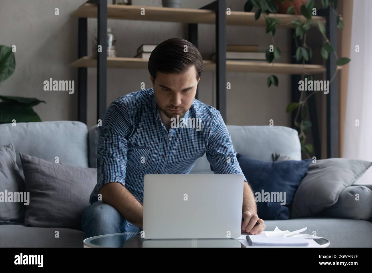 Serious man using laptop, working online, sitting on couch Stock Photo