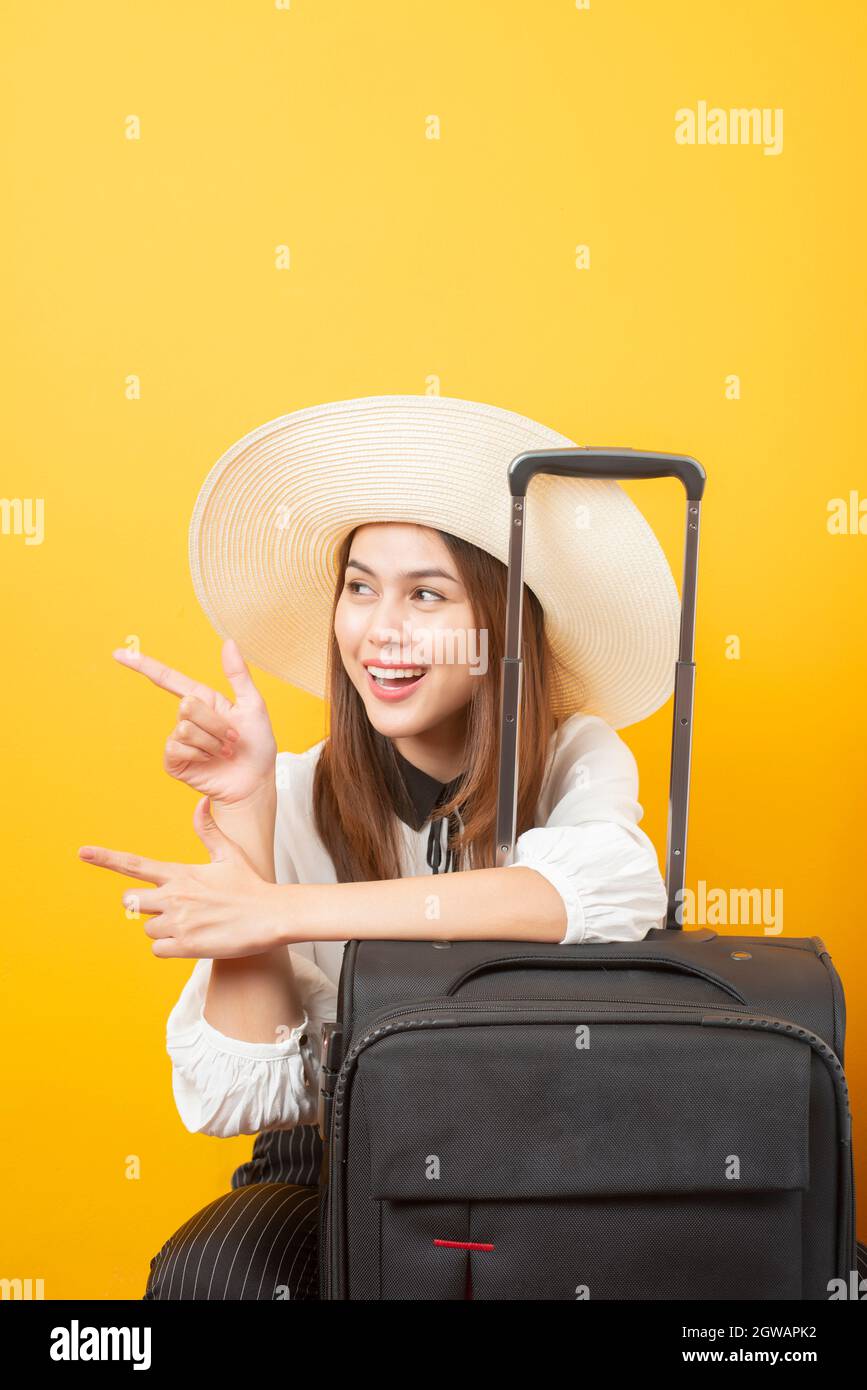 Young Woman Gesturing By Suitcase Against Yellow Background Stock Photo