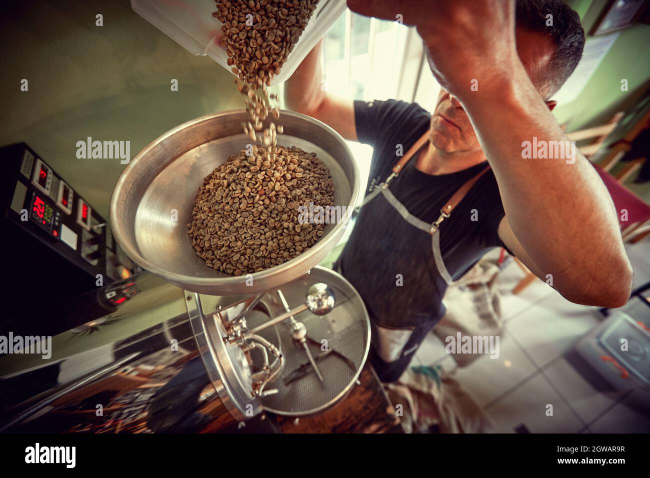 Man drip raw coffee over a coffee roasting machine. Stock Photo