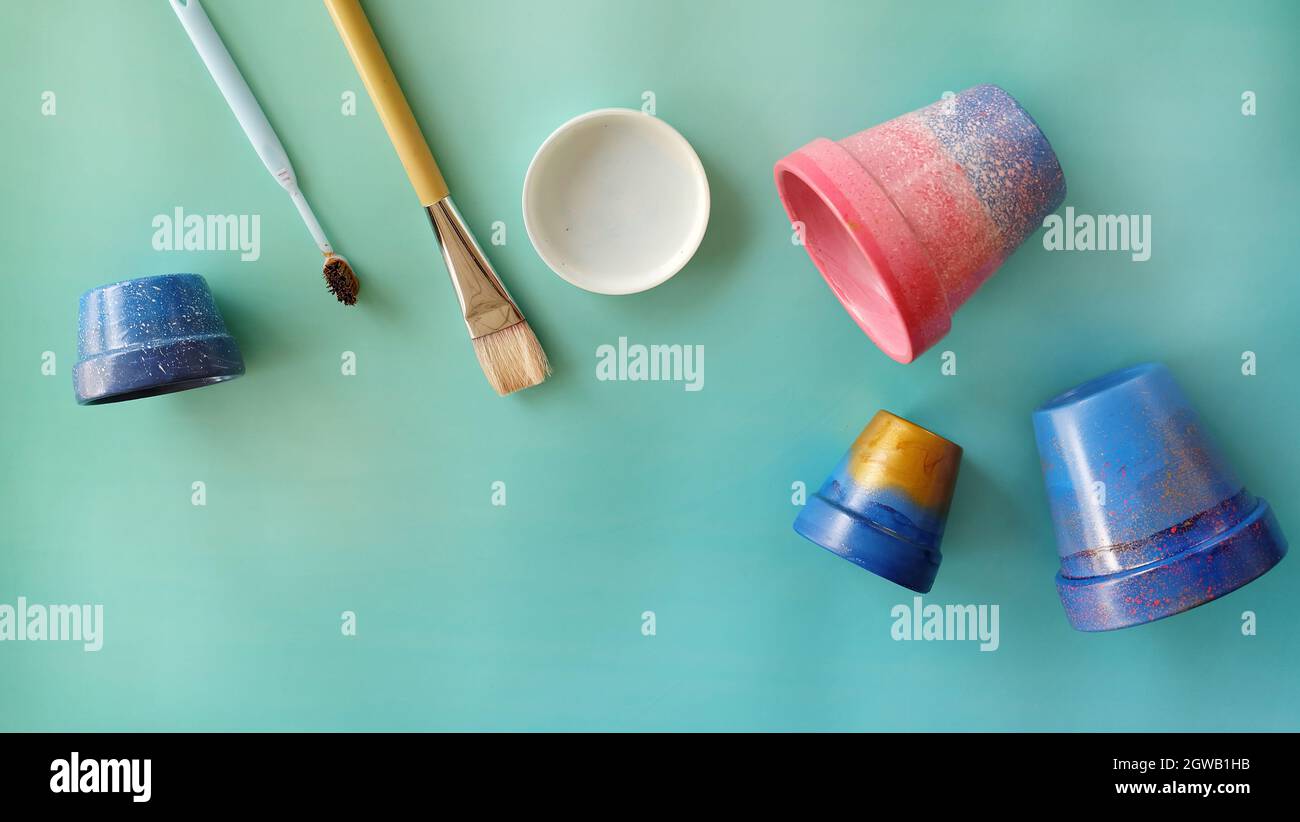 Flat lay of colorful painted terracotta pots, paintbrush, toothbrush and a paint tray. With copy space on the bottom left corner. Stock Photo