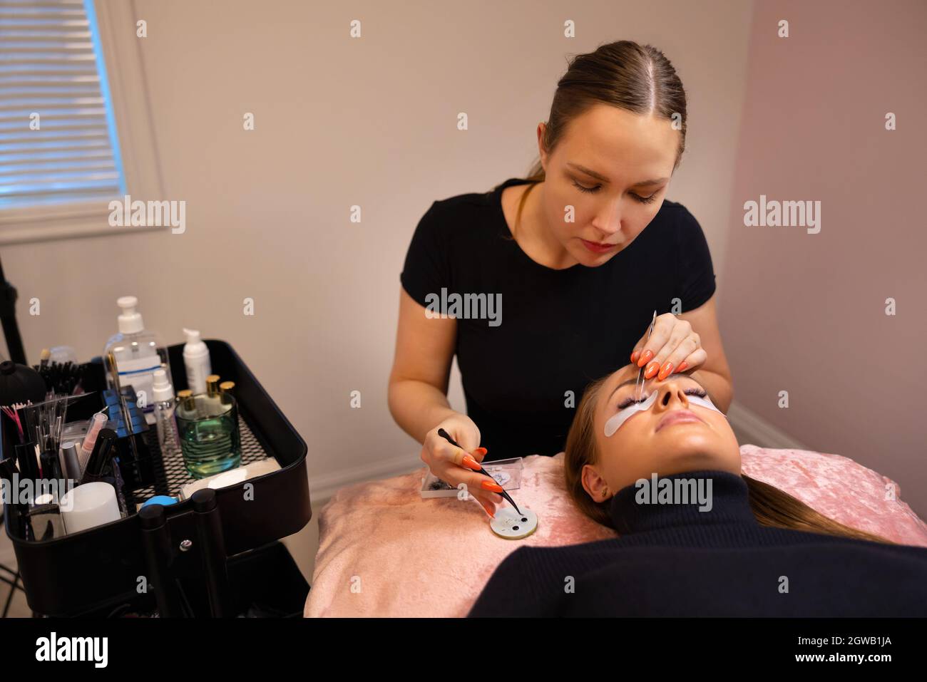 Brunette Beautician Using Tweezers For Eyelash Extension Treatment Stock Photo