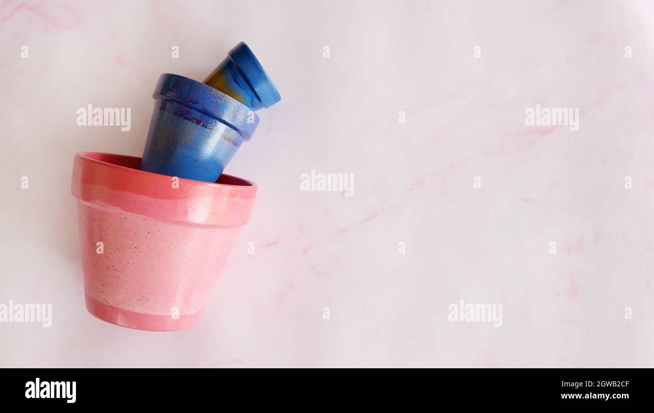 Flat lay of 3 terracotta pots in different sizes, from small to large. Pots are painted in blue and pink acrylic paints, and placed on pink background Stock Photo