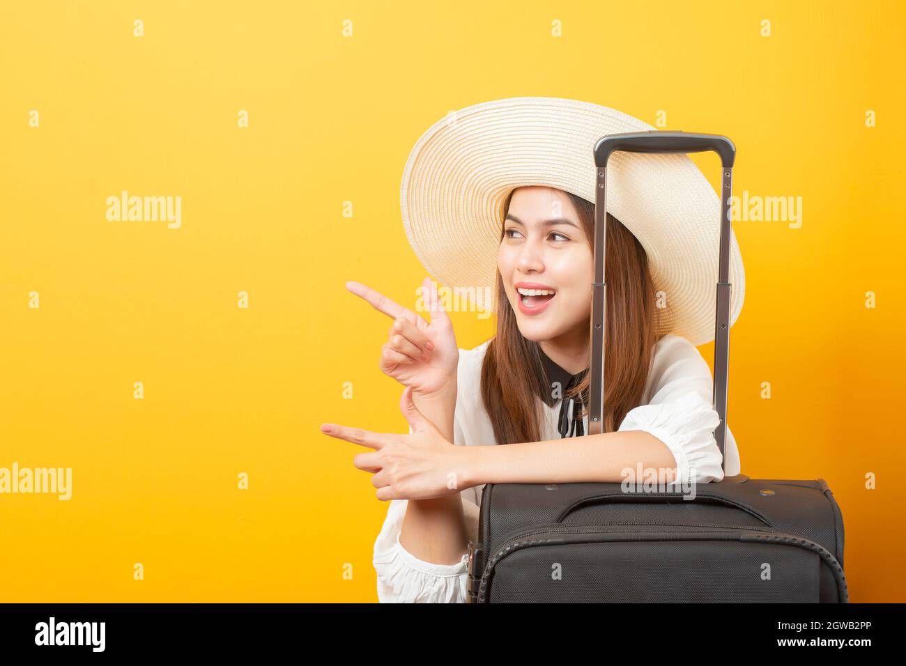 Young Woman Pointing By Suitcase Against Yellow Background Stock Photo