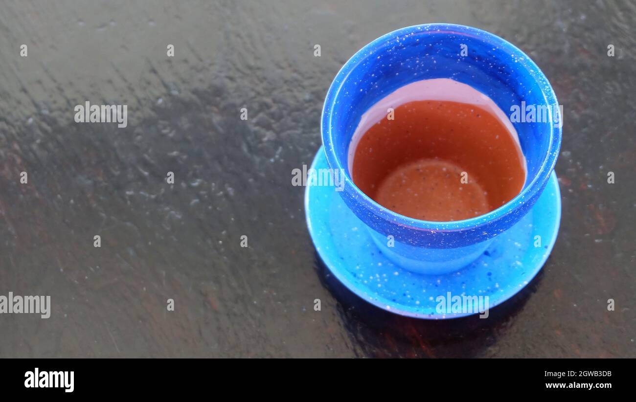 An empty terracotta pot painted in blue, with a blue pot saucer. Placed on a wooden surface, with copy space on the left. Stock Photo