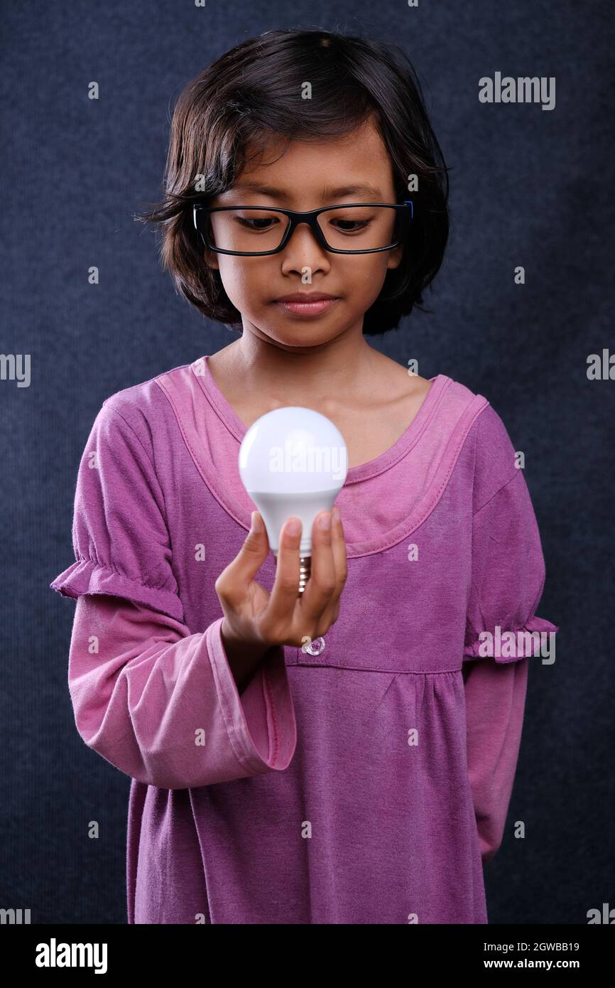 Girl Standing Holding Bulb Against Black Background Stock Photo