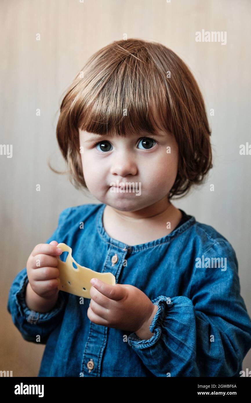 Little baby girl eating cheese. Cute baby enjoy a piece of cheese Stock Photo