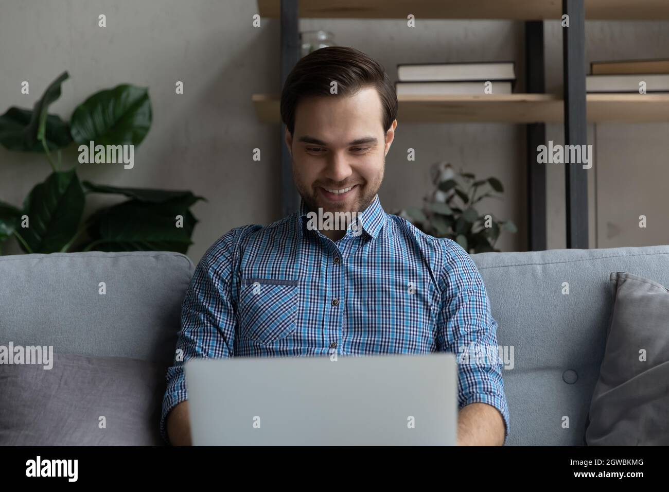 Smiling man using laptop, sitting on couch at home Stock Photo
