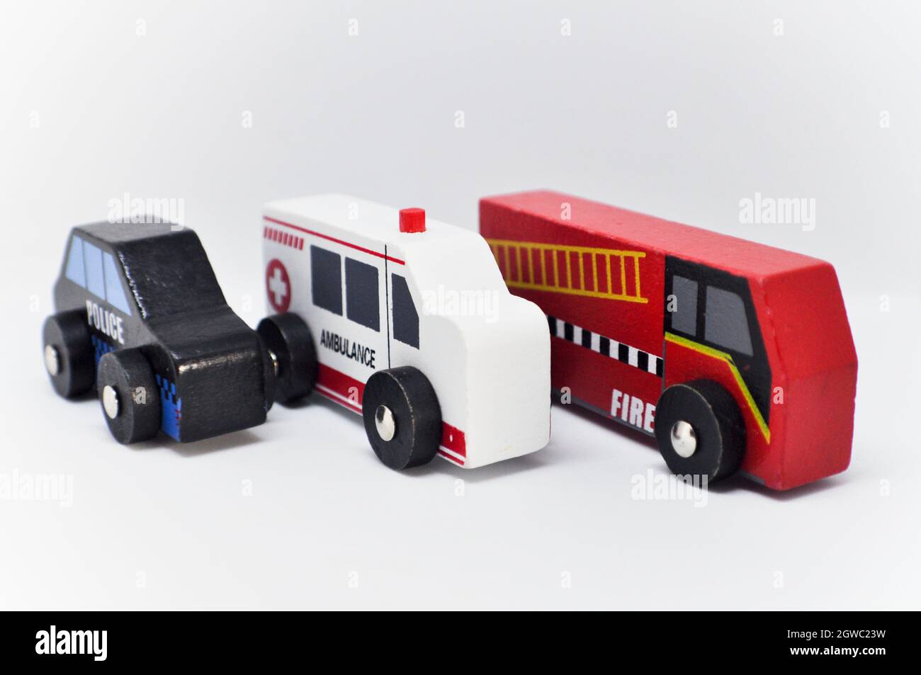 Wooden toy emergency service vehicles set against a white background. The toys are simply made. Police, ambulance and fire engine are lined up Stock Photo