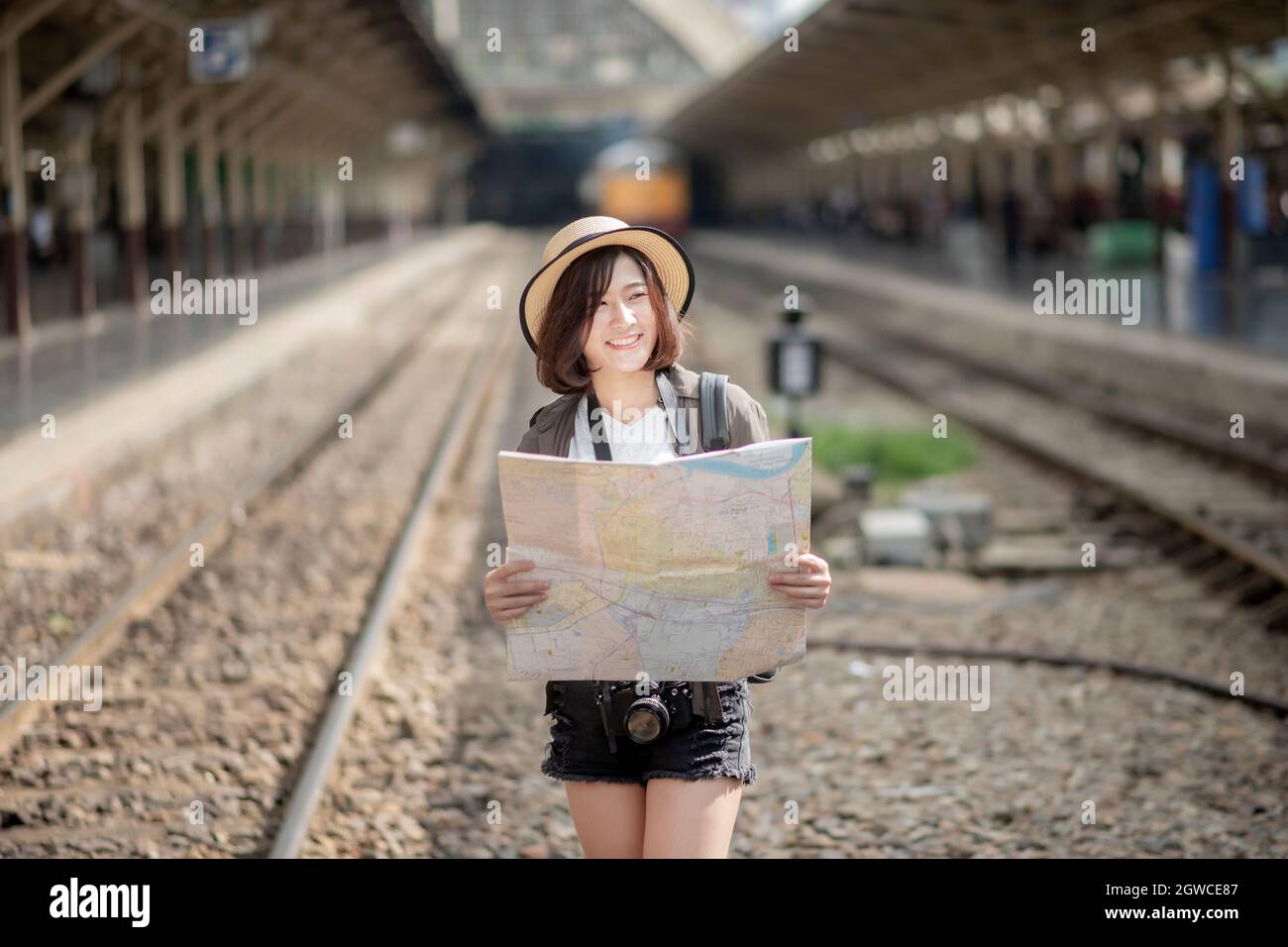Female Tourist Holding Map While Standing On Railroad Track Stock Photo