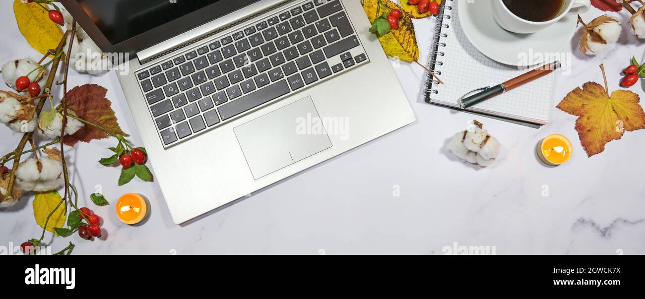 autumn desktop with laptop computer keyboard, notepad, colorful leaves and candles, seasonal home office in panoramic format with copy space, high ang Stock Photo