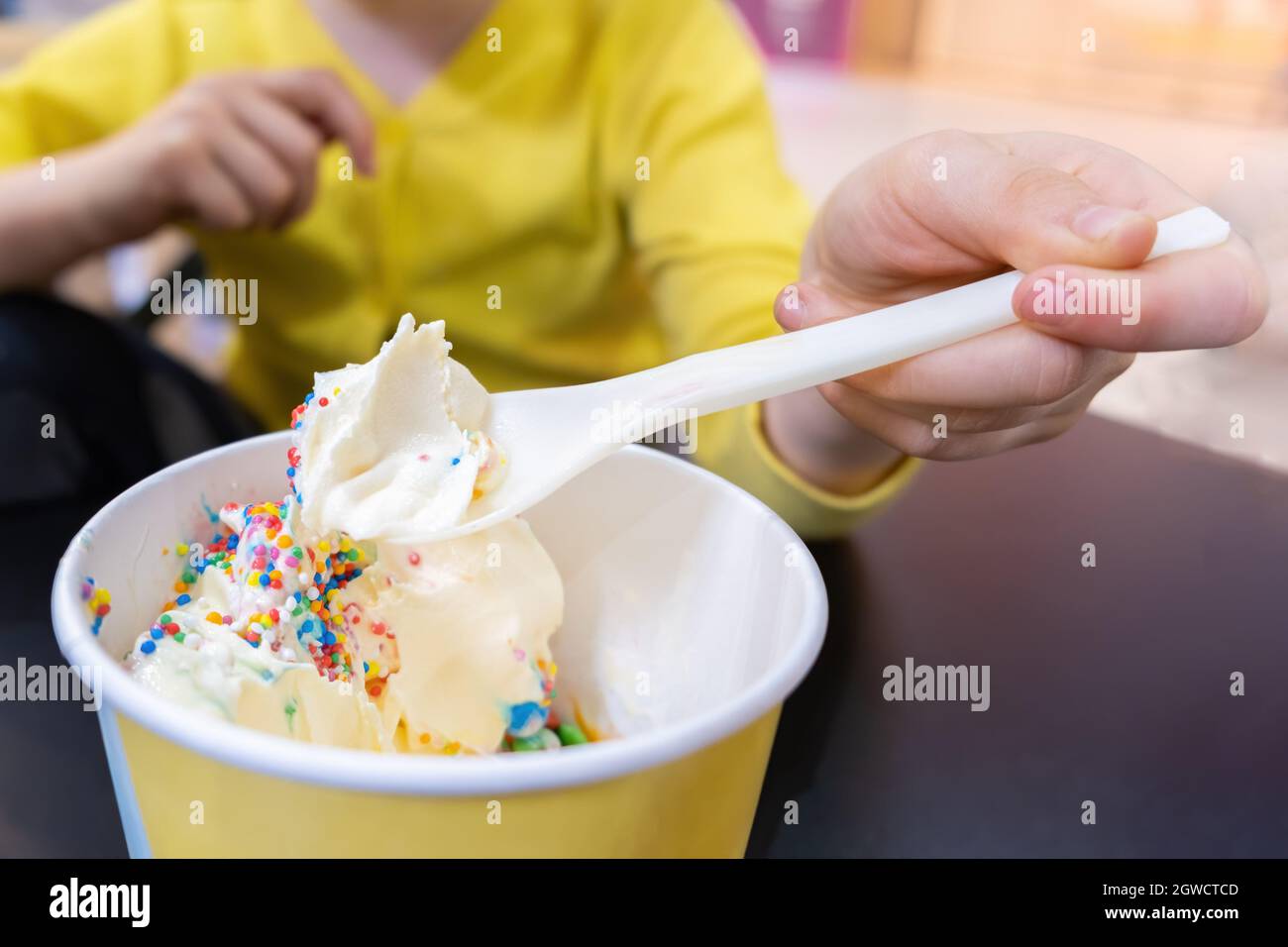 Girl Hand Holding White Plastic Spoon With Sweet Yogurt And Sprinkles - Shallow Focus Stock Photo