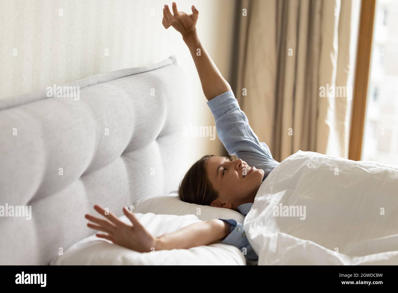 Happy girl awaking in white linen beddings, stretching arms Stock Photo