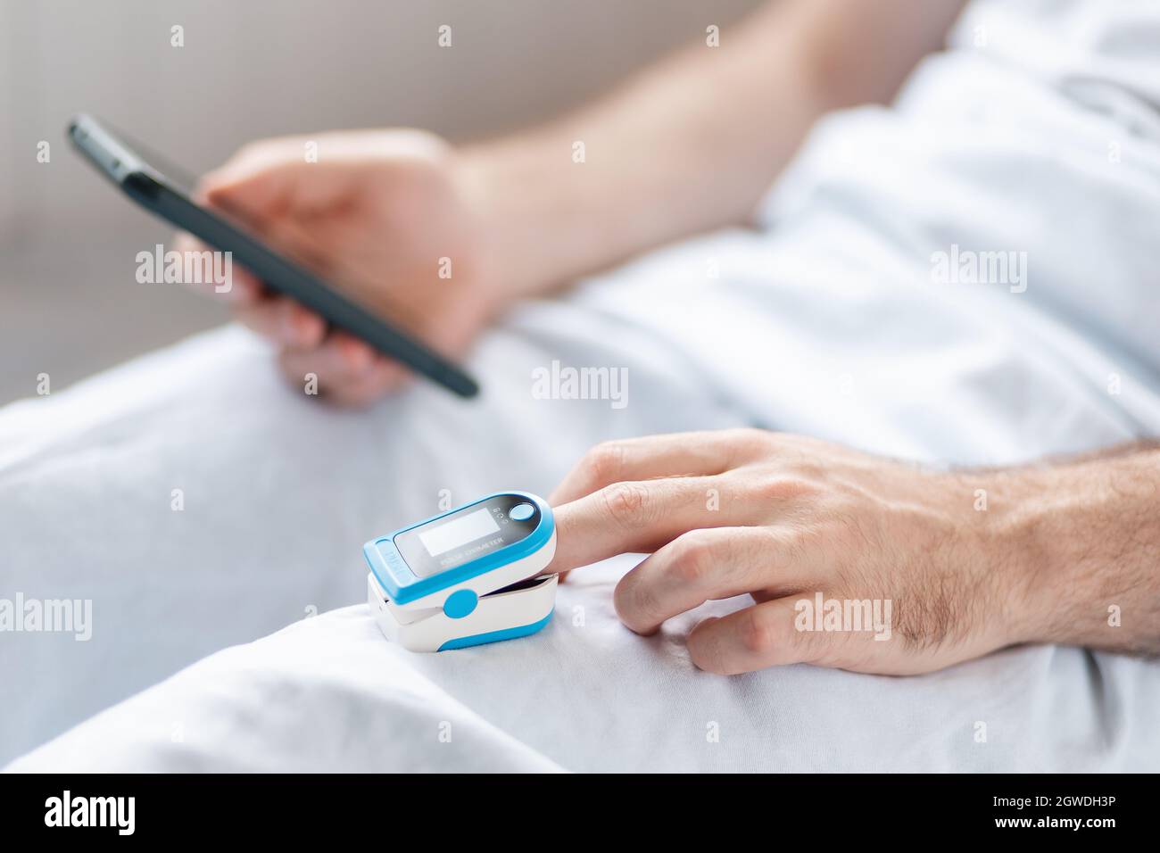 Patient lying at bed with pulse oximeter and using a smartphone with helth care app. Close up of