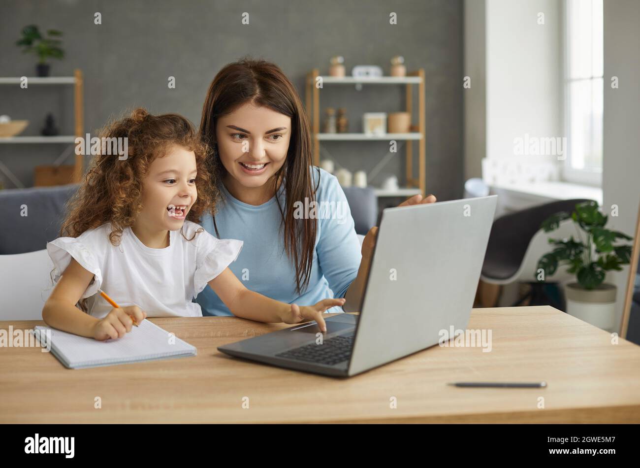 Happy mother and child sitting at desk at home and having online class on laptop Stock Photo