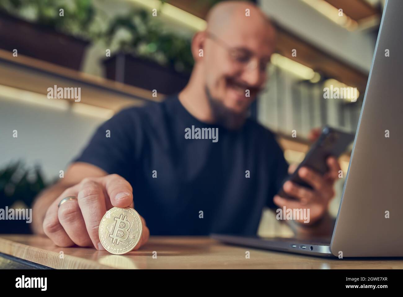 Successful bald businessman holds a gold bitcoin coin in his hand while
