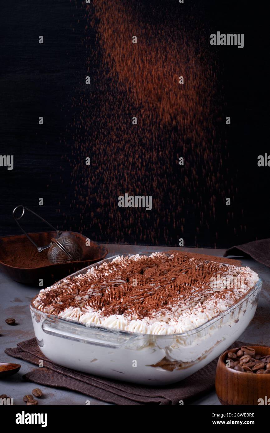 Sprinkling Tiramisu Cake With Cocoa Powder. Italian Dessert. Action Shot Stock Photo